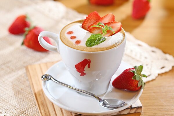 Coffee in a cute cup with foam, mint and strawberries