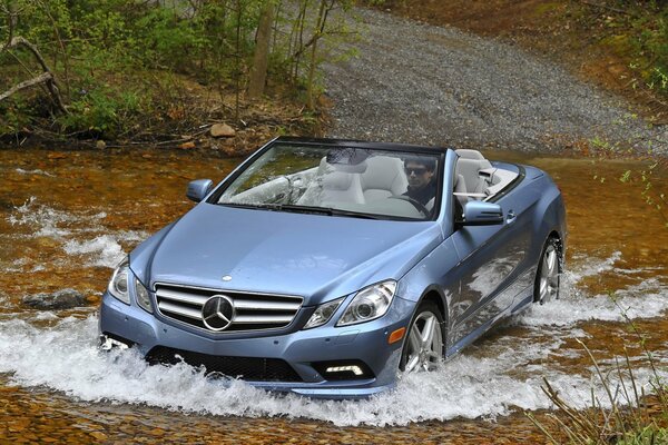 A shiny Mercedes without a driver forces a shallow river