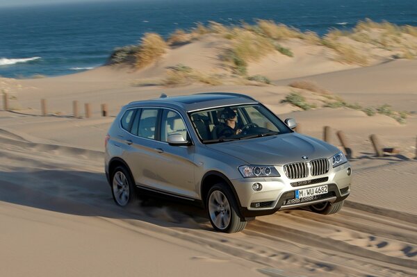 Silberner bmw x3 fährt auf dem Sand vor dem Hintergrund des Meeres