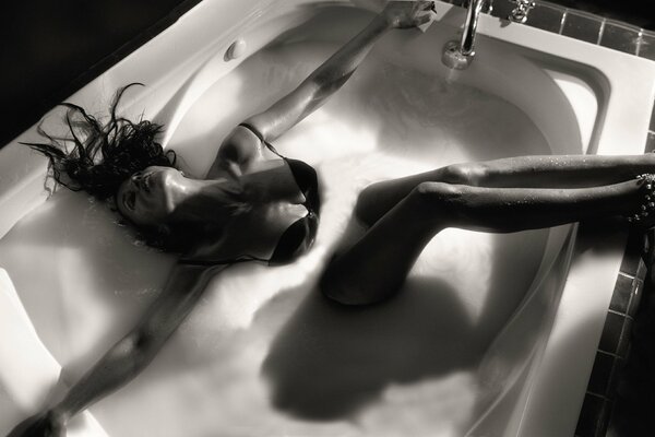 The brunette lies in the bathtub and shows her legs and breasts