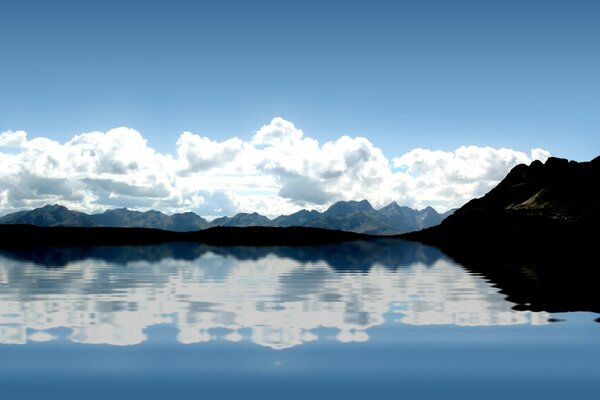 Am See steht das Wasser ruhig und reflektiert Wolken und Berge