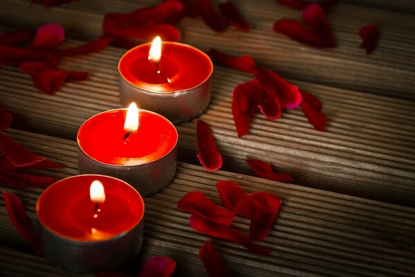 Three red tea candles are lit, red petals are scattered around