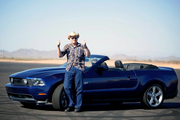 Ein Mann steht in der Nähe eines Ford Mustang Cabrio in blauer Farbe