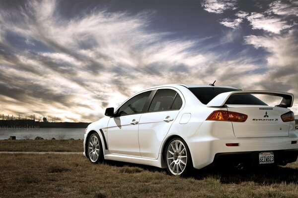 A white Mitsubishi stands against a backdrop of beautiful clouds and a river