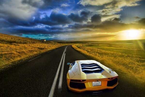 Une Lamborghini jaune roule sur la piste. Autour du paysage avec des champs au coucher du soleil