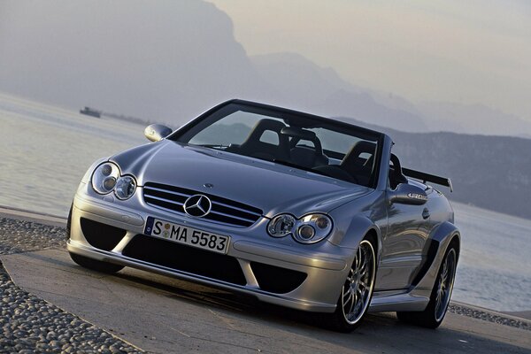 Silberfarbenes Mercedes-Auto auf dem Hintergrund von Wasser und Straße