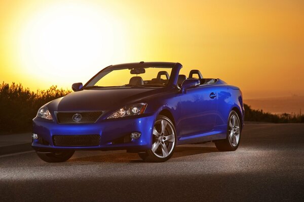 Blue Lexus car on the road in the wasteland against the background of the setting sun