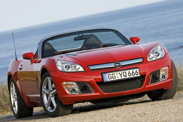 Opel convertible rojo en la orilla cerca de la superficie del agua