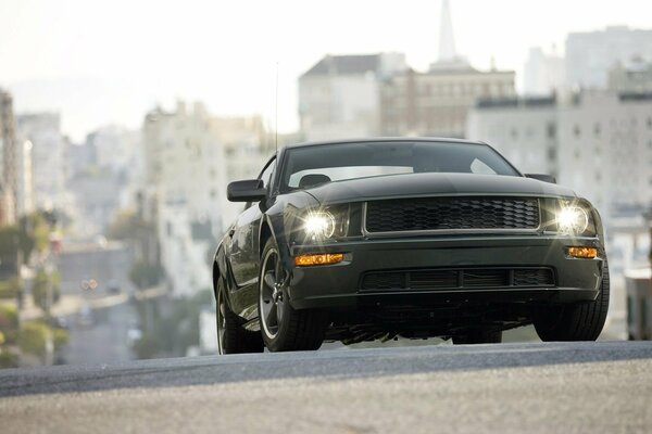 Ford mustang bullitt rushes along the road against the backdrop of urban high-rise buildings