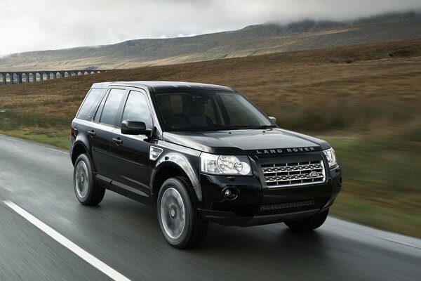 Un land rover noir roule sur une piste de campagne sur fond de collines