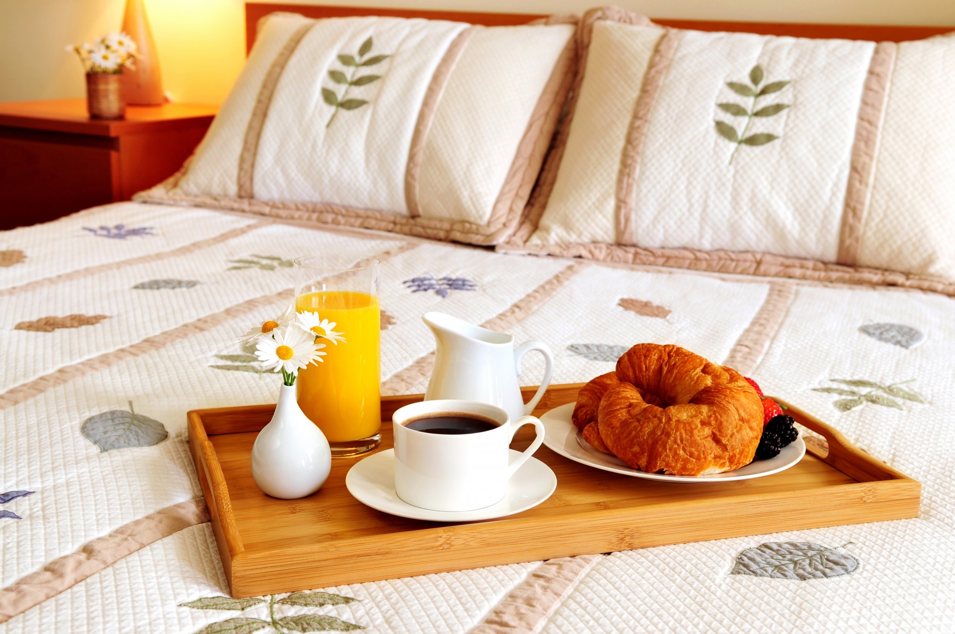 cama bandeja taza café florero flores almohadas jugo