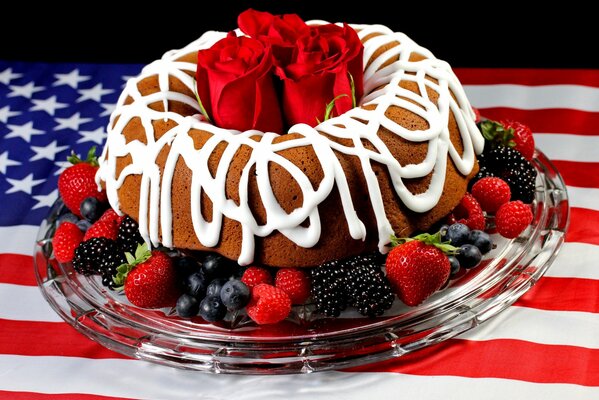 A glass dish with a cake with roses overlaid with fruit