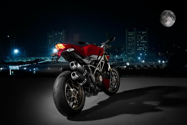 Czerwony motocykl marki Ducati stoi nocą na tle miasta