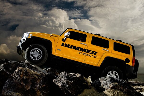 Hummer amarillo en las rocas contra las nubes