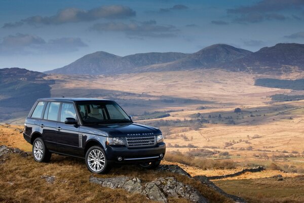 Ein schwarzer Range Rover steht auf einer steilen Klippe vor dem Hintergrund eines schönen Tals