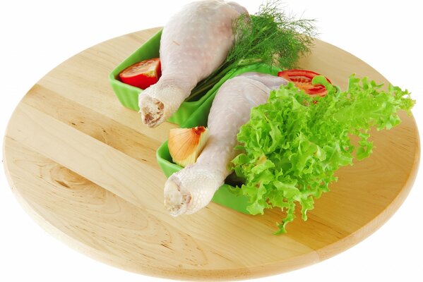 Two chicken legs in trays with vegetables on a round plate