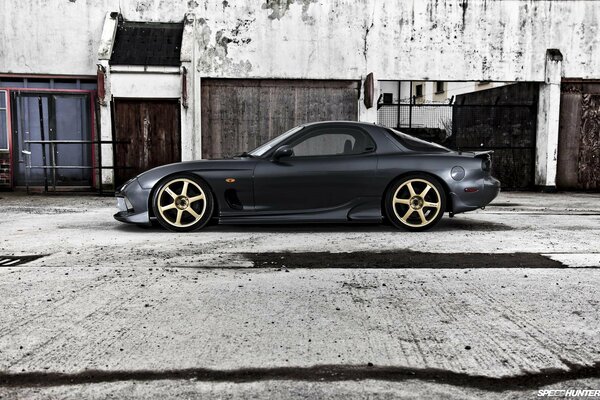 Sporty black Mazda with golden wheels near a concrete building