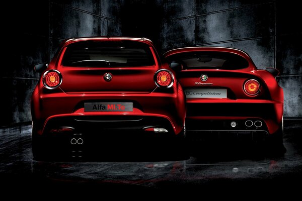 Two red alfa romeos against a gloomy black wall