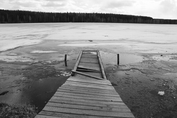 Vieux pont de pêche sur un étang gelé avec vue sur la forêt en noir et blanc