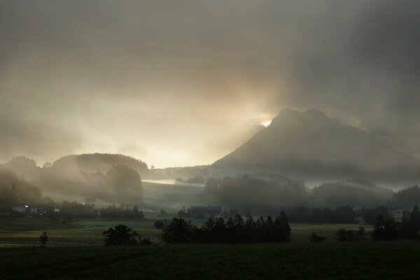 Fog in the mountains over houses and trees. Misty sky over a mountain settlement and trees