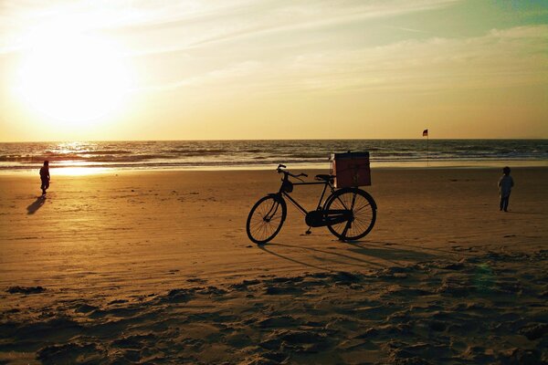 Vélo debout sur la plage de sable de l océan Indien sur fond de soleil couchant