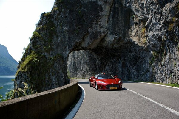 A red car on the road passes an arch