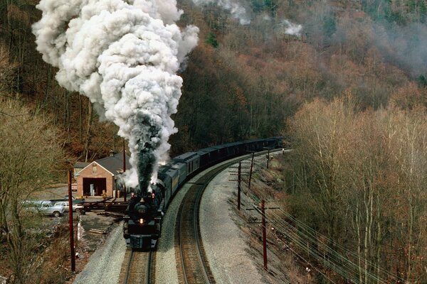 A steam locomotive on the background of an autumn forest with smoke from a chimney