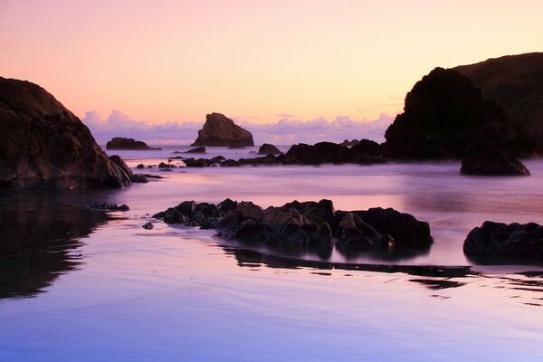 Puesta de sol en el fondo de agua púrpura y piedras