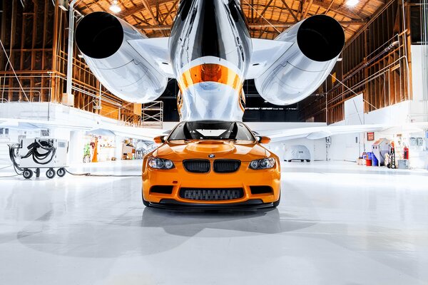 Une BMW orange sous un avion dans un hangar