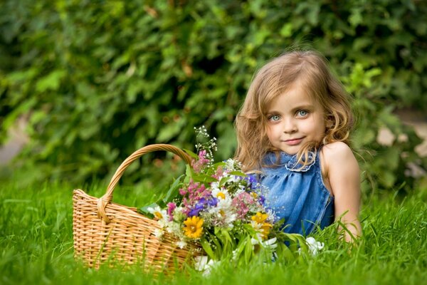 Niña con una cesta de flores de pradera en un césped verde