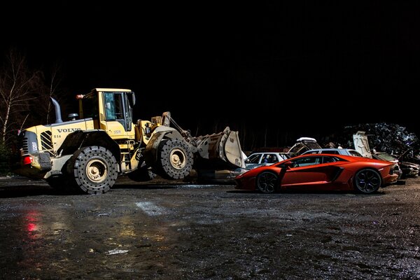 Bulldozer Volvo dans la nuit avec une Lamborghini orange