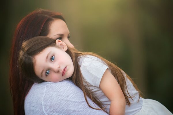 Ein blauäugiges Mädchen liegt kopfüber auf der Schulter ihrer Mutter