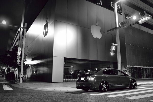 Black and white photo of a car near the apple building