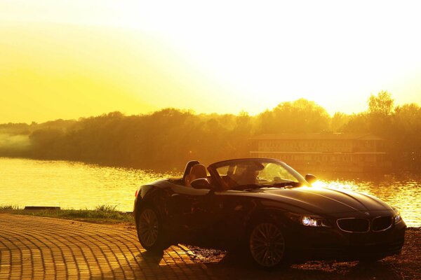 The cabriolet is standing on the bank of the river bathed in the sun