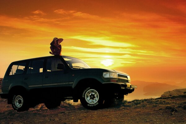 Mädchen auf dem Dach eines Jeeps auf dem Hintergrund des Sonnenuntergangs