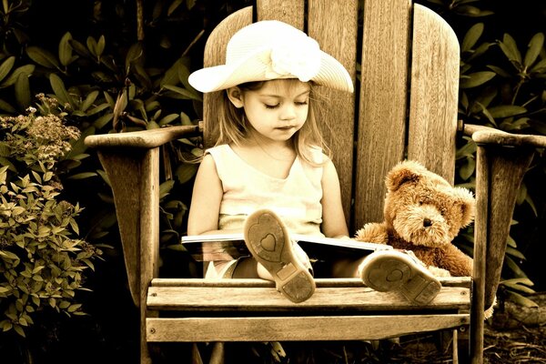Fotografía en sepia. Una niña con un sombrero con un oso. Niña sentada en una silla alta con un libro y otro oso de peluche
