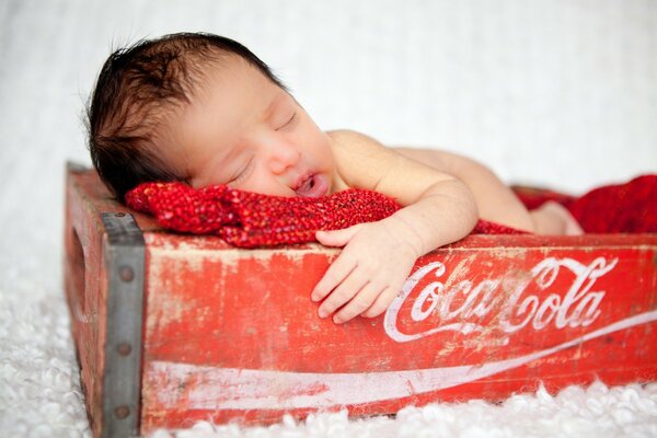 Schlafendes Baby in einer Coca-Cola-Kiste. Baby auf einer roten Decke