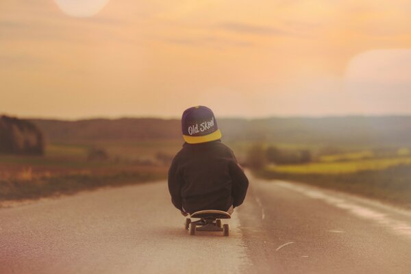 Ein Junge auf einem Skateboard schaut in den Sonnenuntergang. Schöner roter Sonnenuntergang. Ein Junge mit einer Kappe fährt auf der Straße