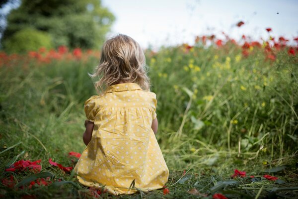 Una niña pequeña en un vestido amarillo de verano se sienta en un Prado