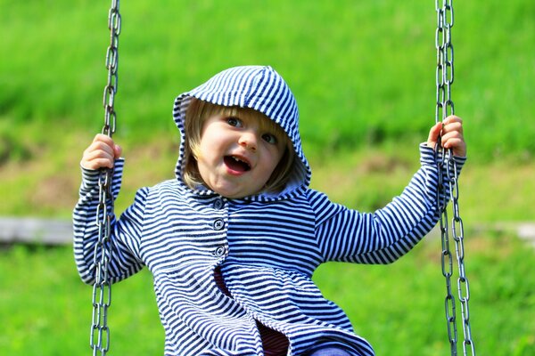 L enfant se balance sur une balançoire. Jolie fille souriante mouche