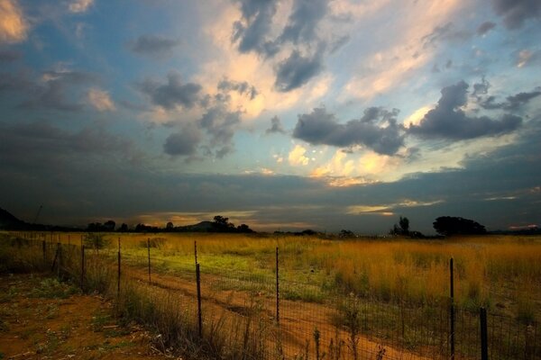 Zaun am Abend unter dicken Wolken