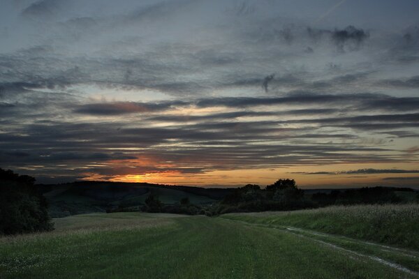 Camino que conduce a las colinas. Puesta de sol con nubes