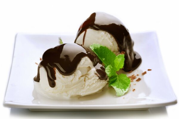 Two balls of ice cream on a plate doused with chocolate with mint leaves