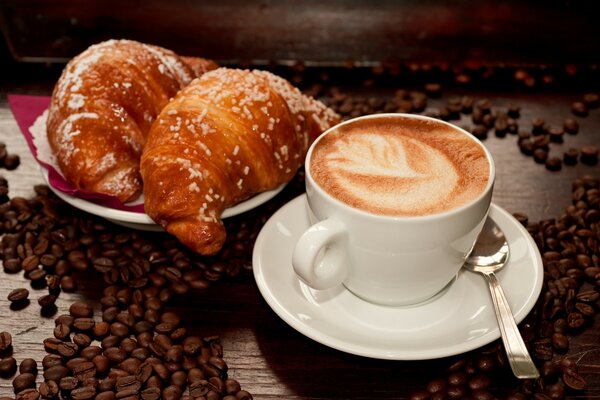 Croissants mit einer Tasse Kaffee auf einem Hintergrund von Kaffeebohnen