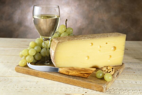 Vino bianco in un bicchiere con un pennello di uva e formaggio delizioso