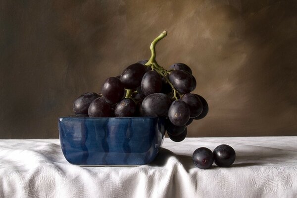 Nature morte de raisins Noirs dans un bol bleu, sur une nappe blanche