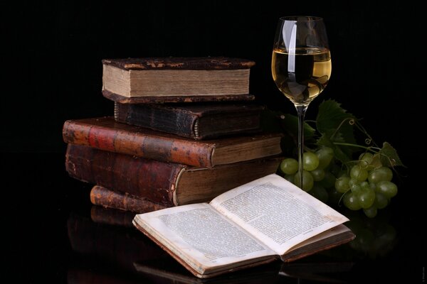 Pile de livres, livre ouvert, vin et raisins verts sur la table