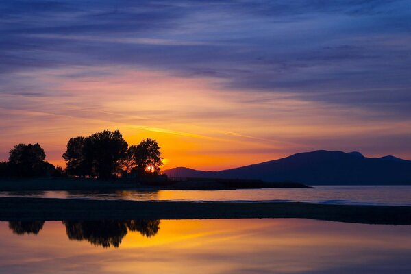 Coucher de soleil orange sur la rive au pied des montagnes