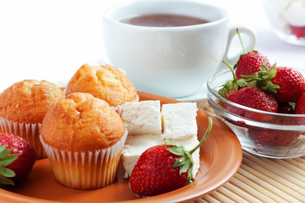 Muffins und Erdbeeren auf einem Teller . Auf dem Hintergrund einer Tasse Tee