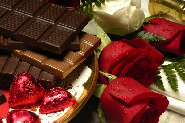 Chocolates, chocolate bars next to a bouquet of roses